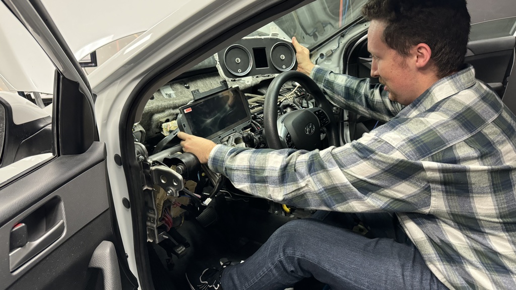 Reichert sits in the half-cab and holds the original Sonata gauge cluster in his right hand and holds the new digital gauge cluster in his left hand